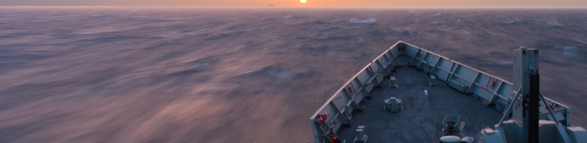 A ship sailing into a beautiful sunset, viewed from the front of another ship.
