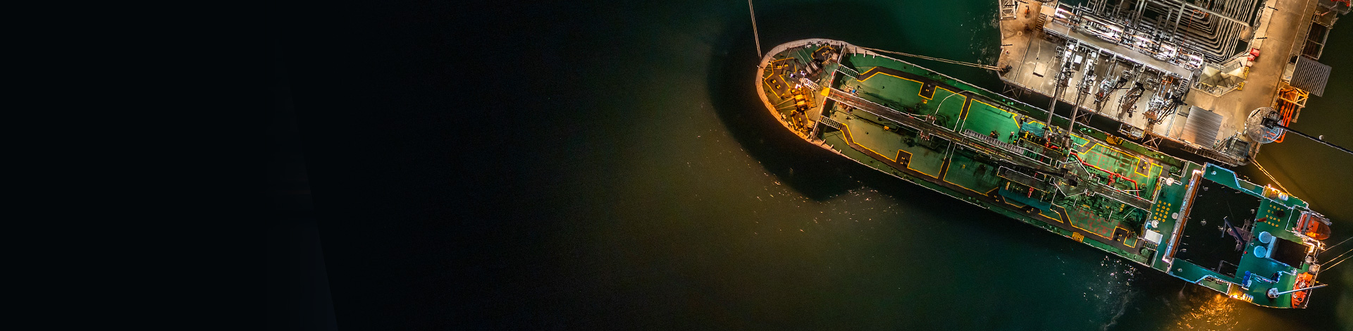 Aerial view of a large vessel docked at night with illuminated areas highlighting intricate details of the deck and equipment.