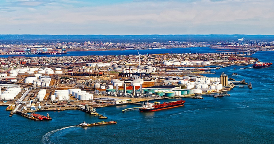 Aerial view of a busy industrial port area with multiple storage tanks and ships, highlighting the extensive infrastructure against a coastal backdrop.
