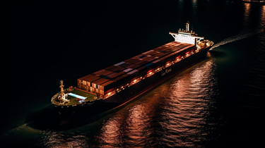 An aerial view of a cargo ship illuminated against the dark night sky, sailing through the vast ocean.