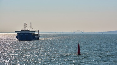 A large blue boat floating near a red buoy in the water.