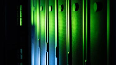 Dark server room with glowing green lights shining on metallic surfaces.
