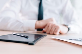 Close-up of a businessman’s hands using a tablet and a pen on a sleek desk.