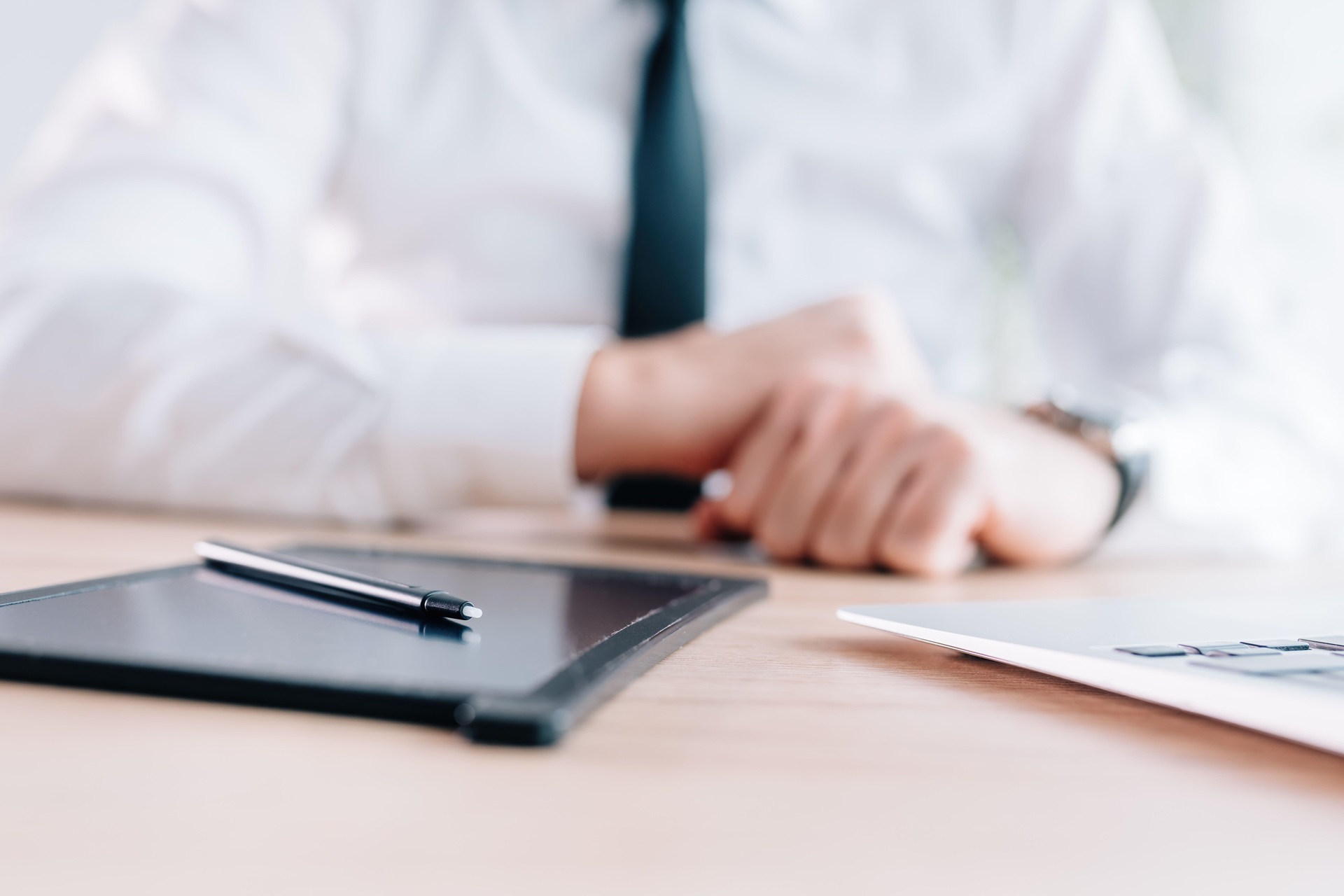 Close-up of a businessman’s hands using a tablet and a pen on a sleek desk.