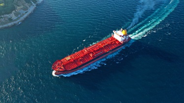 An aerial view of a red cargo ship sailing in the vast ocean, transporting goods across the waters.
