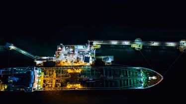 Aerial view of ship at night, illuminated by lights, sailing on dark waters.